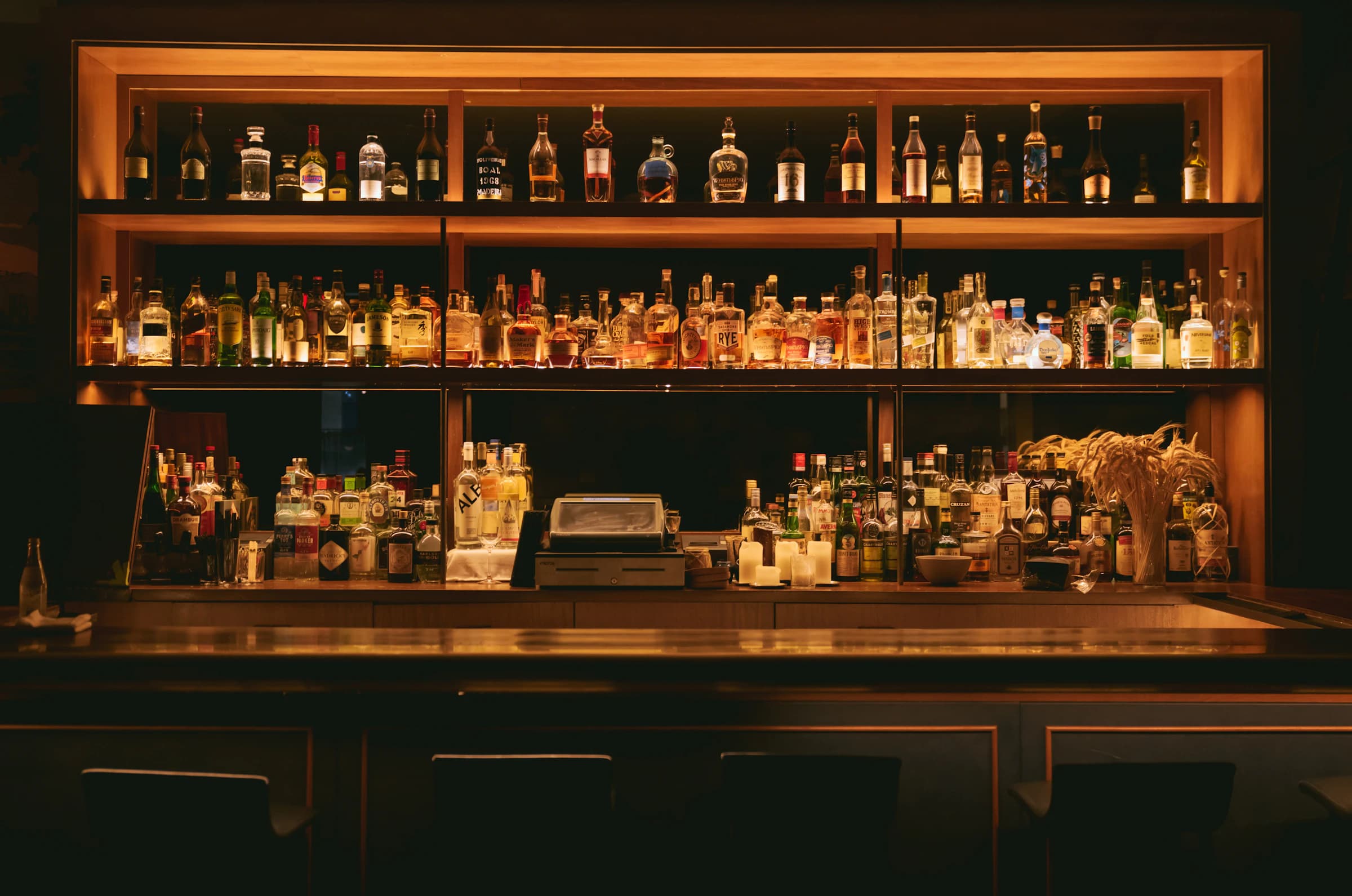 A dimly lit, elegant bar backed by rows of illuminated spirit bottles